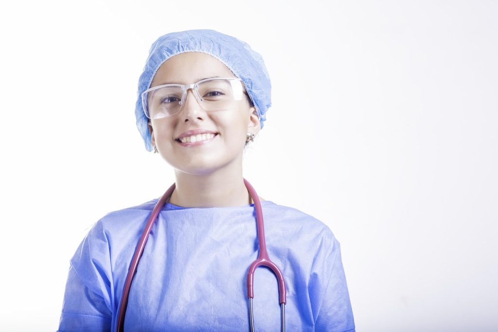 Smiling nurse in blue scrubs with protective glasses and a stethoscope – Nursing Assignment Help UK.